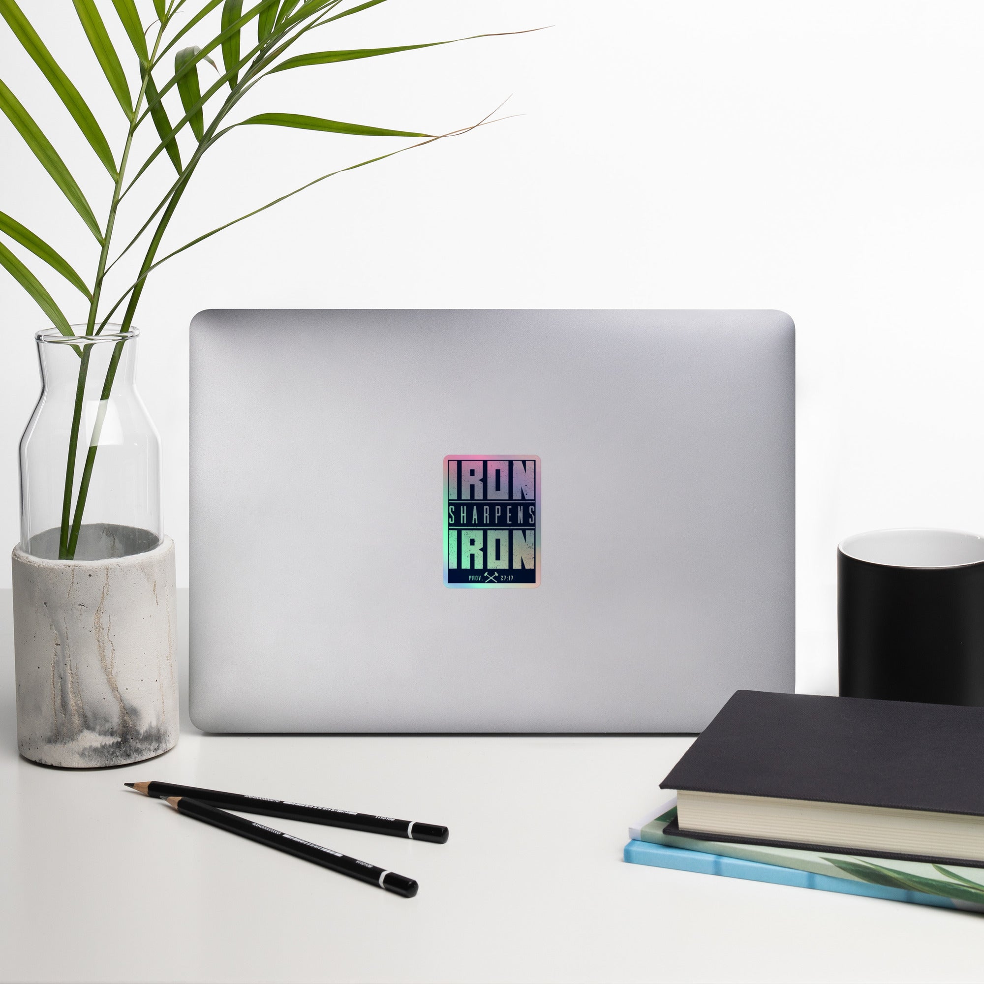 A rectangular vinyl holographic sticker with the text 'IRON SHARPENS IRON' in white on a navy blue background, applied to a Silver Computer.