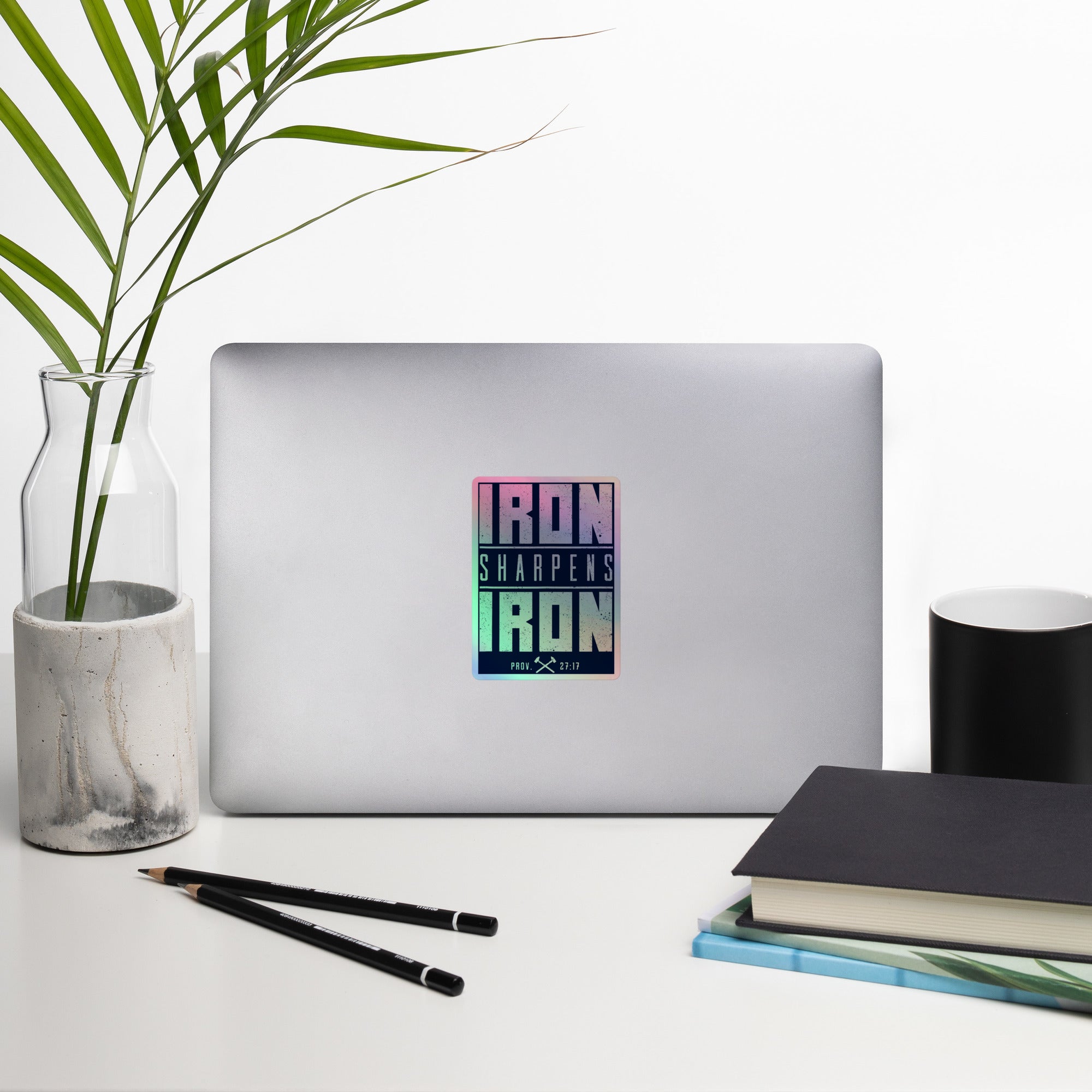 A rectangular vinyl holographic sticker with the text 'IRON SHARPENS IRON' in white on a navy blue background, applied to a Silver Computer.