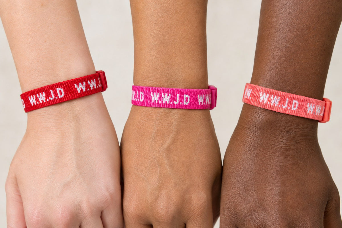 WWJD woven bracelets in red, hot pink, and coral worn on three wrists
